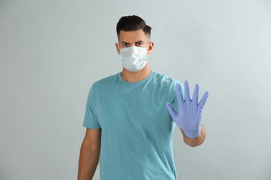 Man in protective face mask and medical gloves showing stop gesture on grey background