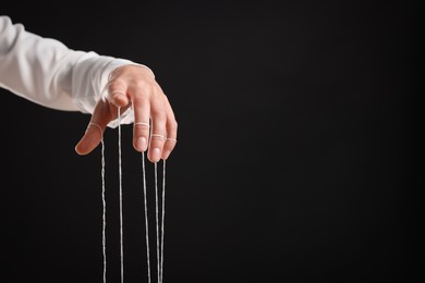 Woman pulling strings of puppet on black background, closeup. Space for text