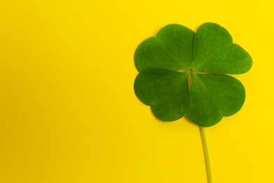 Beautiful green four leaf clover on yellow background, top view. Space for text