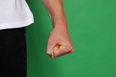 Young man showing fist on green background, closeup. Aggression concept