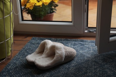 Stylish door mat and slippers on wooden floor indoors