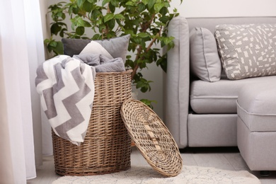 Basket with blankets and pillow near sofa indoors