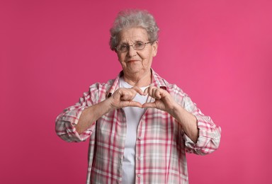Elderly woman making heart with her hands on pink background