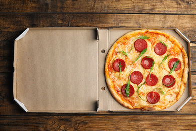 Tasty pepperoni pizza in cardboard box on wooden table, top view