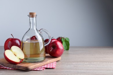 Jug of tasty juice and fresh ripe red apples on wooden table, space for text
