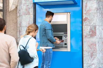 Photo of Young people standing in queue to cash machine outdoors