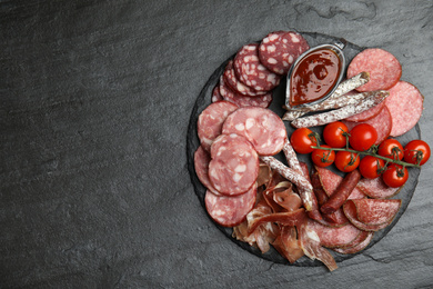 Different types of sausages with tomatoes served on black table, flat lay