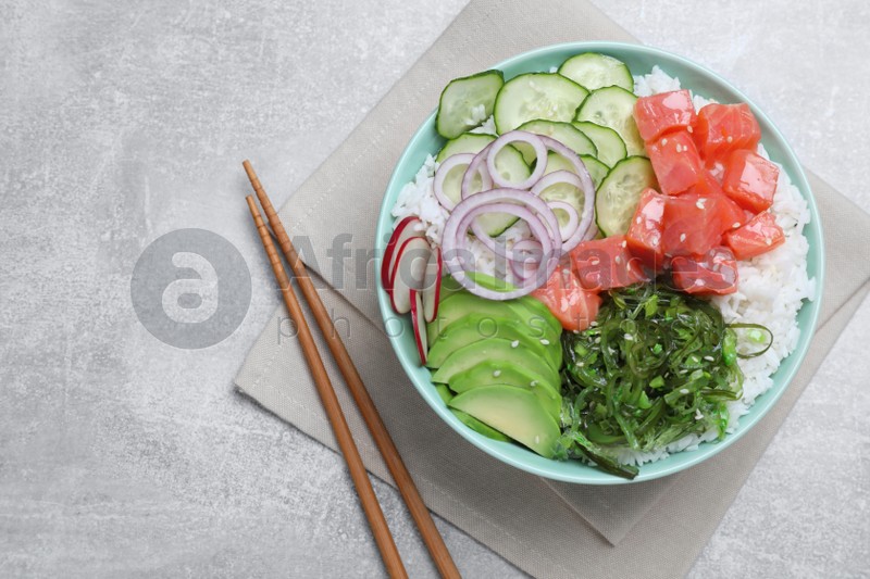 Delicious poke bowl with salmon, seaweed and vegetables served on light grey table, flat lay