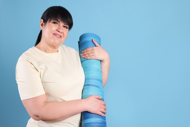 Happy overweight mature woman with yoga mat on light blue background, space for text