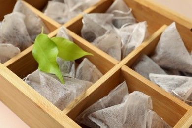 Photo of Many tea bags in wooden box and leaves, closeup
