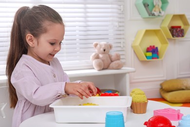 Cute little girl playing with bright kinetic sand at table in room