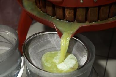 Grape juice pouring from wooden wine press into bucket indoors, closeup