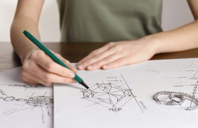 Photo of Jeweler drawing sketch of diamond on paper at table, closeup