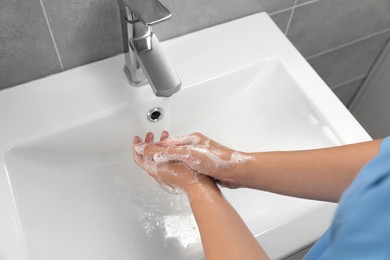 Doctor washing hands with water from tap in bathroom, above view
