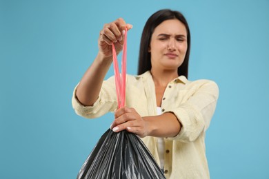 Woman holding full garbage bag against light blue background, focus on hand