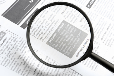 Looking through magnifying glass at newspaper, closeup. Job search concept