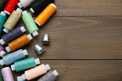 Photo of Colorful threads and sewing thimbles on wooden table, flat lay. Space for text