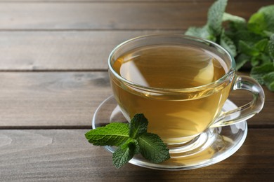 Photo of Cup of aromatic green tea with fresh mint on wooden table. Space for text
