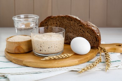 Photo of Glass jar with sourdough and other ingredients for bread on white wooden table