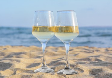 Photo of Glasses of tasty wine on sand near sea