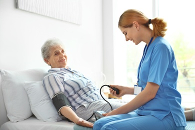 Nurse measuring blood pressure of elderly woman indoors. Medical assistance