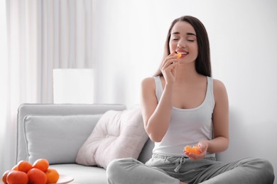 Happy young woman eating ripe tangerine at home