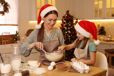 Mother with her cute little daughter making dough for Christmas cookies in kitchen
