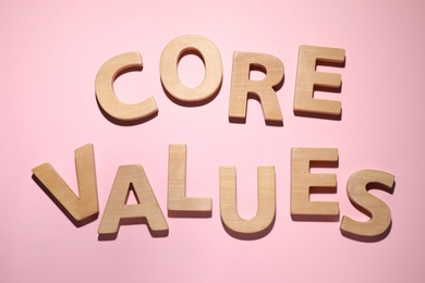 Photo of Phrase CORE VALUES made of wooden letters on pink background, flat lay