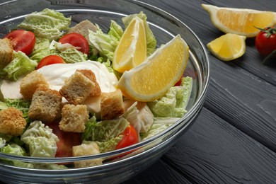 Bowl of delicious salad with Chinese cabbage, lemon, tomatoes and bread croutons on black wooden table, closeup