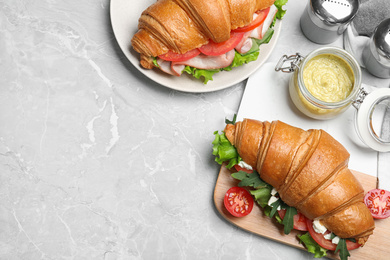 Flat lay composition with tasty croissant sandwich on light grey marble table. Space for text