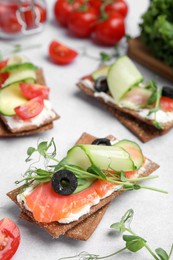 Tasty rye crispbreads with salmon, cream cheese and vegetables on light grey table
