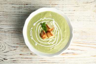 Delicious broccoli cream soup with croutons served on white wooden table, top view