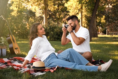 Man taking picture of his girlfriend on picnic plaid in summer park
