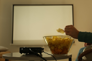 Man eating chips while watching movie using video projector at home, closeup