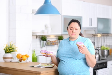Pensive overweight woman with donuts in kitchen. Failed diet