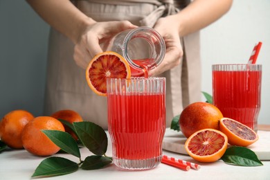 Woman pouring tasty sicilian orange juice into glass at white wooden table, closeup