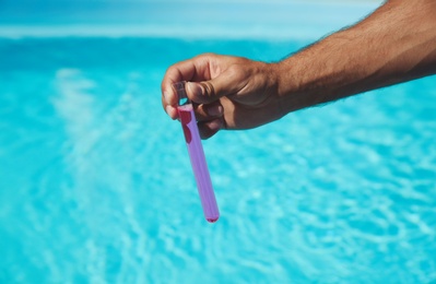 Man holding test tube with reagent near swimming pool, closeup
