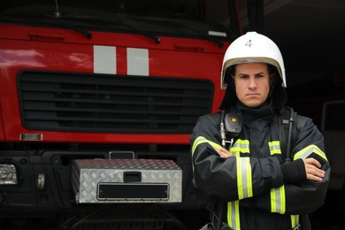 Portrait of firefighter in uniform and helmet near fire truck at station, space for text