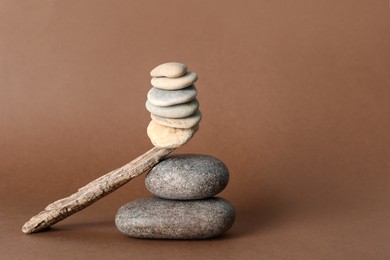Stack of stones balancing on wooden stick against brown background, space for text. Harmony concept