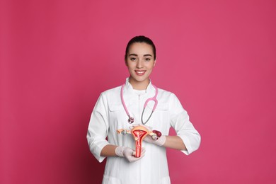Doctor demonstrating model of female reproductive system on pink background. Gynecological care