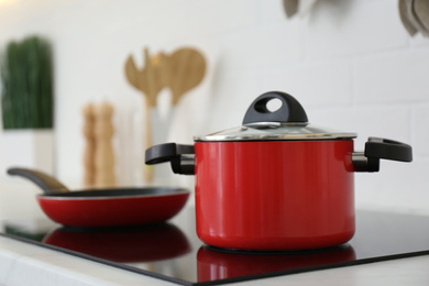 Red pot and frying pan on stove in kitchen, closeup