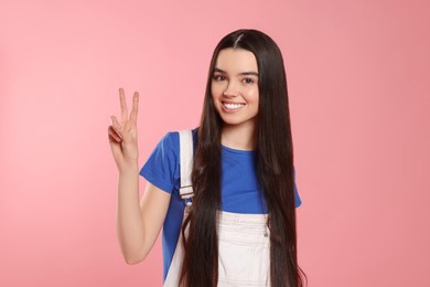 Photo of Teenage girl showing peace sign on pink background