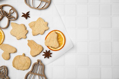 Photo of Baked biscuits of different shapes and cookie cutters on white textured table, flat lay. Space for text