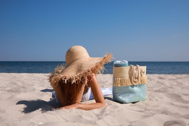 Woman with beach bag and straw hat lying on sand near sea