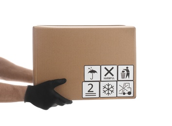 Courier holding cardboard box with different packaging symbols on white background, closeup. Parcel delivery