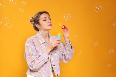 Young woman blowing soap bubbles on yellow background, space for text