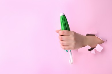 Woman holding closed small green umbrella through hole in light pink paper, closeup. Space for text