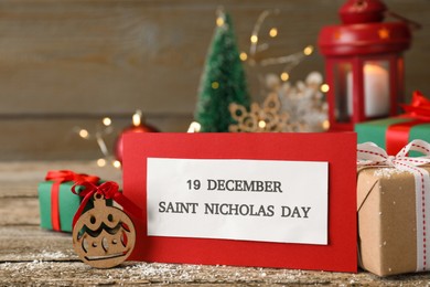 Card with text 19 December Saint Nicholas Day and festive decor on wooden table