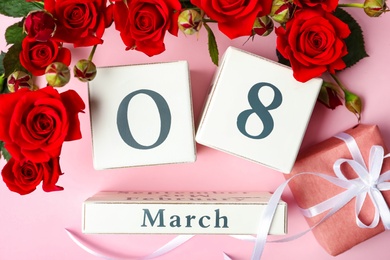 Wooden block calendar with date 8th of March, gift and roses on pink background, flat lay. International Women's Day