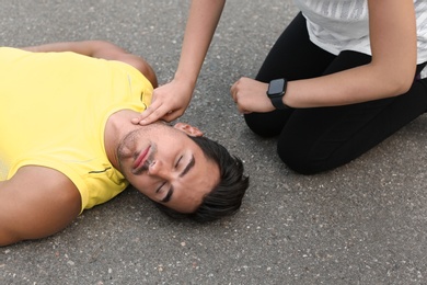 Young woman checking pulse of unconscious man on street